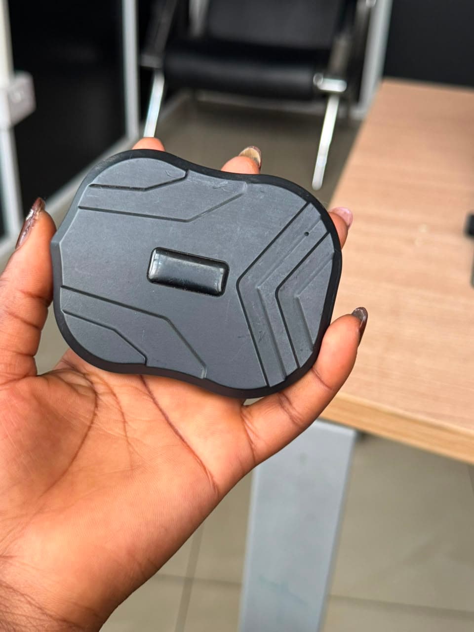 Magnetic-mount GPS tracker held in hand, showing the underside mounting face
